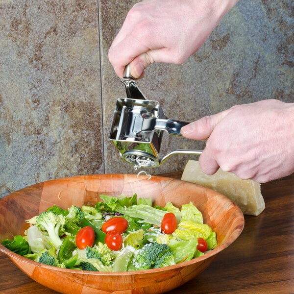 A person using an American Metalcraft stainless steel hand held rotary cheese grater to add cheese to a bowl of salad.