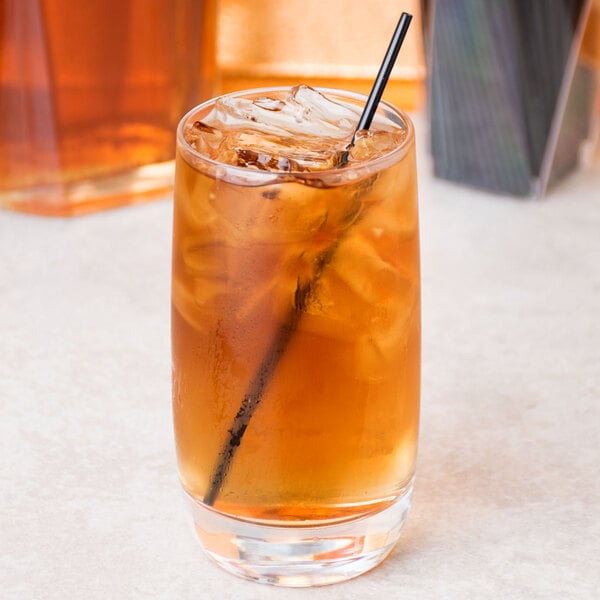 A Chef & Sommelier highball glass with brown liquid, ice, and a straw.