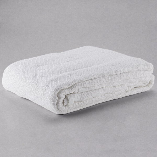 A white Oxford full size thermal hotel blanket folded up on a gray surface.