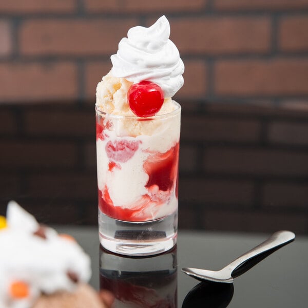 An Arcoroc shot glass filled with red and white liquid, ice cream, and whipped cream with a cherry on top.