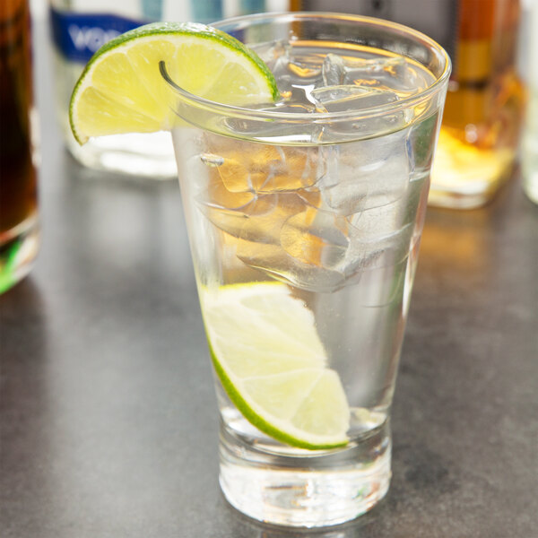 A close up of a Arcoroc Shetland highball glass of water with ice and a lime wedge.