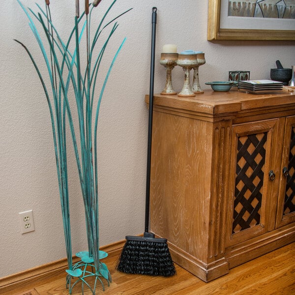 A Carlisle warehouse broom with black bristles leaning against a cabinet.