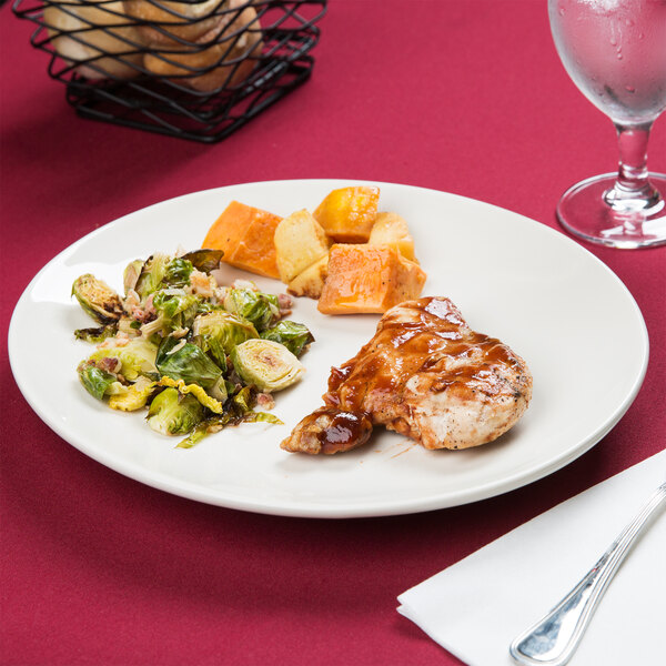 A Tuxton Venice oval china platter with chicken and brussels sprouts on a table.