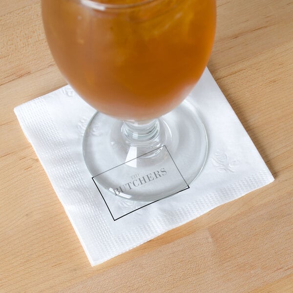 A glass of orange liquid on a white Choice beverage napkin.
