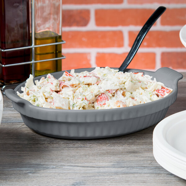 A gray Tablecraft shallow oval casserole dish filled with food on a table.