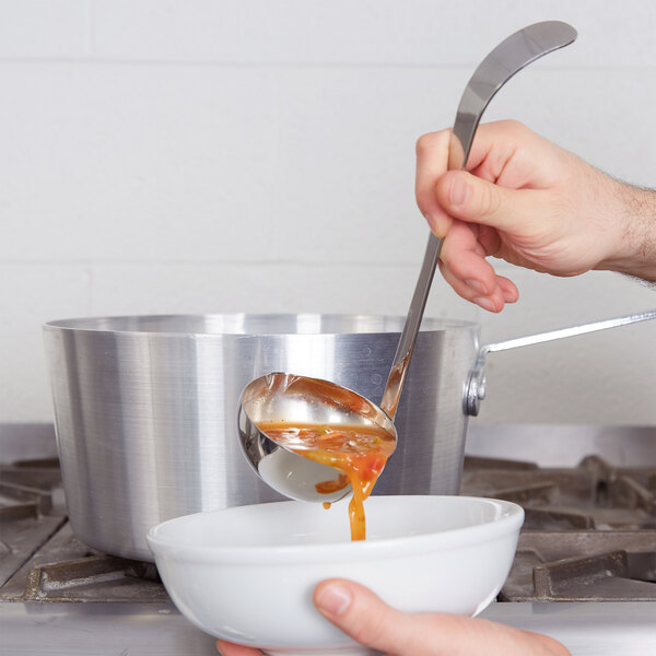 A hand holding a Vollrath stainless steel ladle pouring soup into a bowl.
