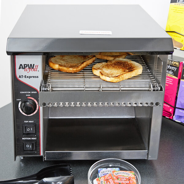 An APW Wyott commercial conveyor toaster with toasted bread on a conveyor.