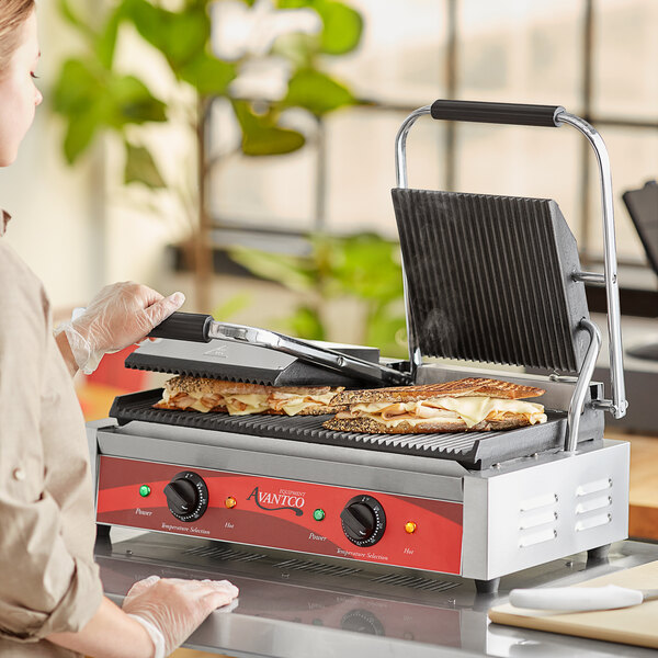 A woman using an Avantco double commercial panini grill to cook a sandwich.