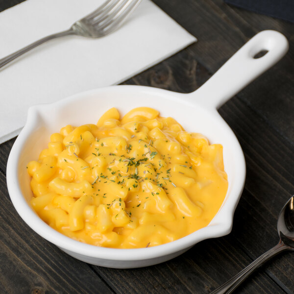 A white cast aluminum fry pan with a bowl of macaroni and cheese.