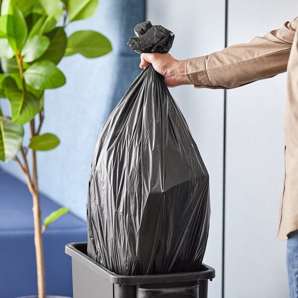 A person putting an Inteplast Group black can liner into a trash can.
