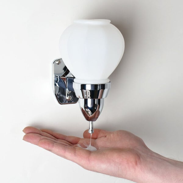 A person's hand using a white wall-mounted Cambro soap dispenser.