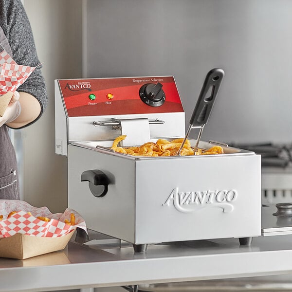 A woman using an Avantco electric countertop fryer to cook french fries.