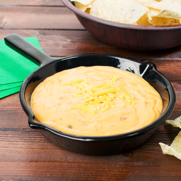 A black Tablecraft fry pan filled with cheese dip next to a bowl of tortilla chips.