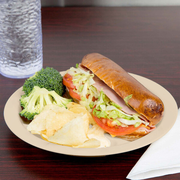 A Cambro beige polycarbonate narrow rim plate with a sandwich, chips, and vegetables.