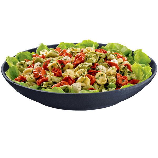 A Tablecraft cast aluminum pasta bowl filled with tortellini on a table with lettuce, red and green peppers, and tomatoes.
