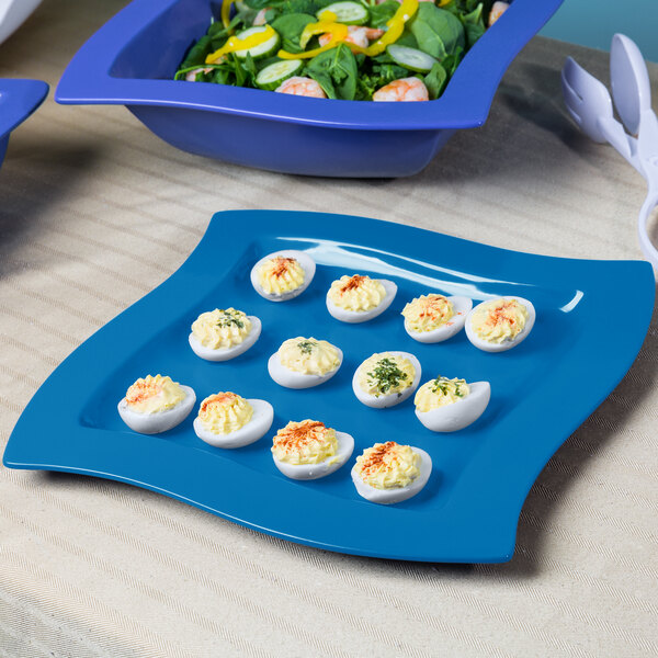 A Tablecraft sky blue metal platter with deviled eggs next to a bowl of salad.