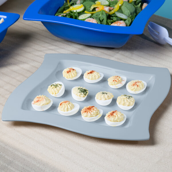 A gray Tablecraft square platter with deviled eggs and salad on a counter.