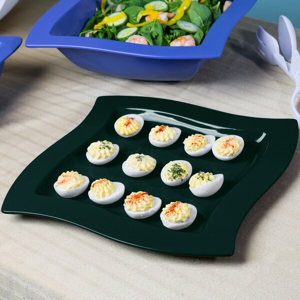 A Tablecraft hunter green and white speckled metal platter with deviled eggs and salad on it.