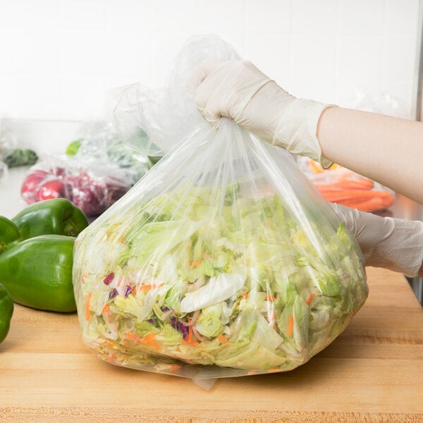 A gloved hand holding a plastic bag of lettuce and carrots.