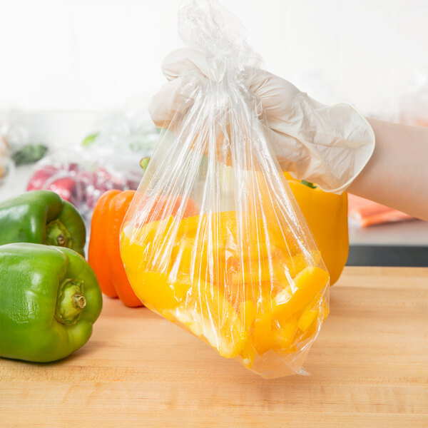 A gloved hand holding a yellow Inteplast Group plastic food bag of yellow peppers.