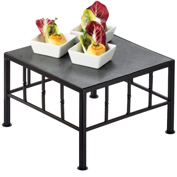 A Cal-Mil black iron square riser with slate top displaying food on a table.