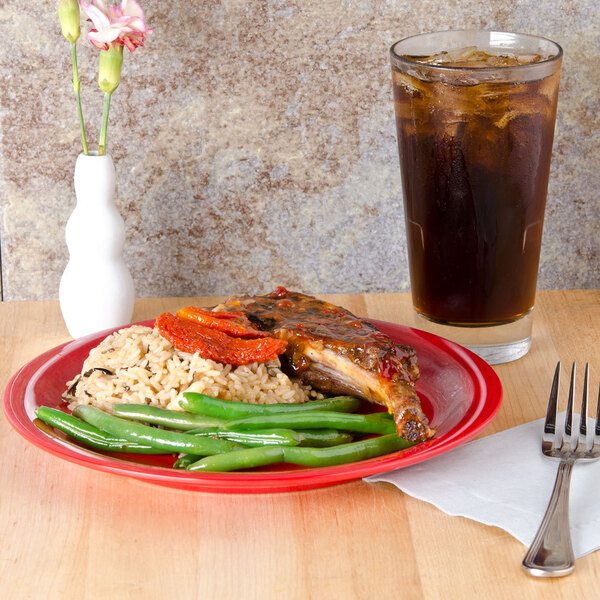 A red Sensation narrow rim plate with rice, beans, and green beans on it on a table.