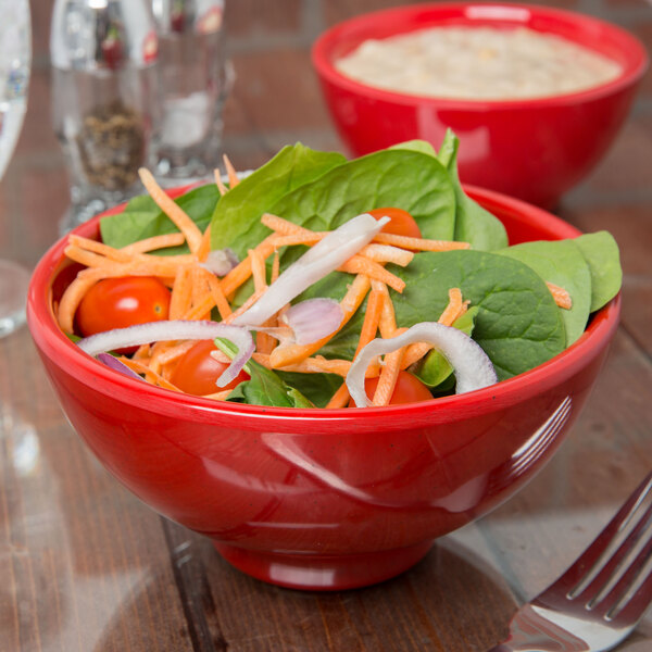 A red Sensation melamine serving bowl filled with salad and vegetables with a fork.