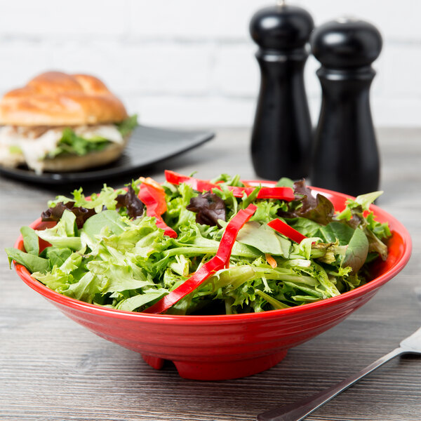 A red GET Melamine bowl filled with salad on a table with a sandwich.