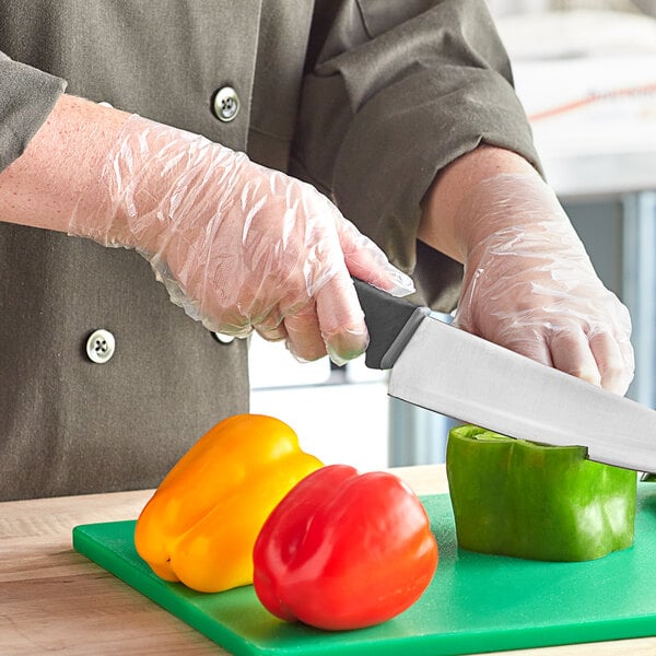 A person in a white coat using Choice disposable gloves to cut red and yellow bell peppers.