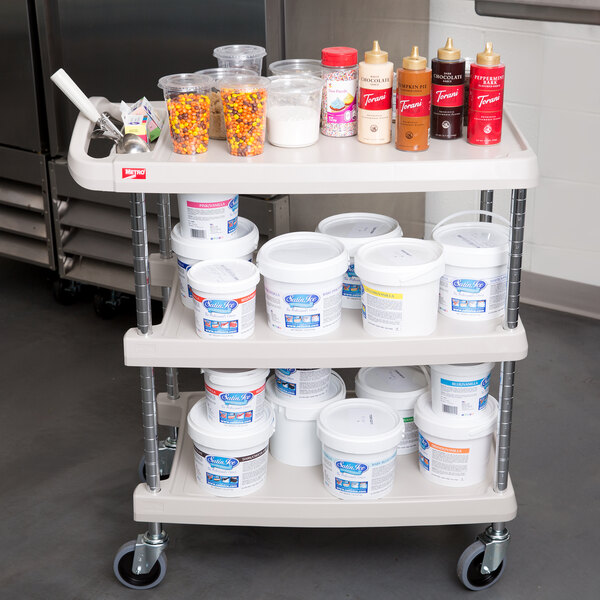 A gray Metro utility cart with three shelves and chrome posts holding food items.