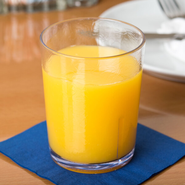A clear Cambro plastic tumbler filled with orange juice on a table.