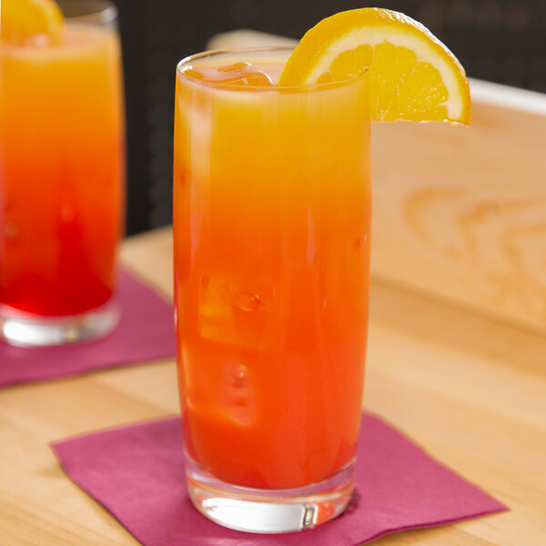A Spiegelau Soiree longdrink glass filled with orange and red liquid with a slice of orange on top.