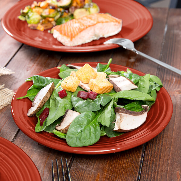 A Fiesta® Scarlet luncheon plate with salad and fish on a table with a fork.