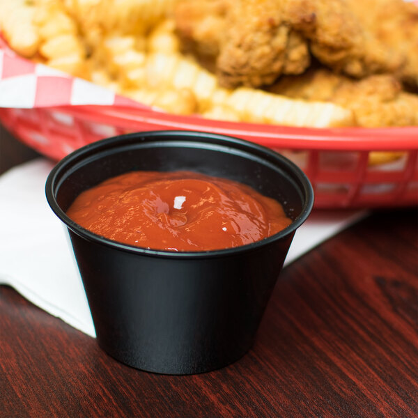 A bowl of ketchup next to fries on a table.