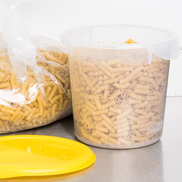 A Rubbermaid translucent plastic food storage container filled with pasta next to a yellow lid.