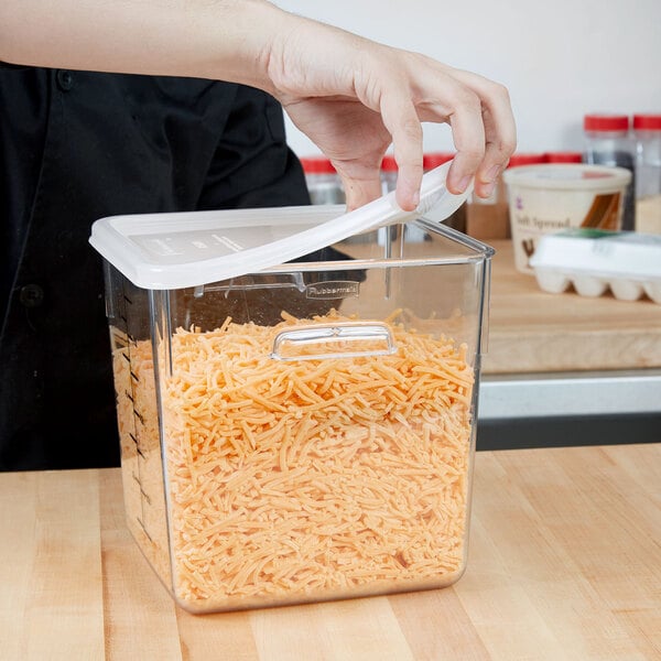 A person putting a Rubbermaid white plastic lid on a container of shredded cheese.