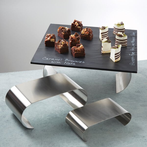A black rectangular table with a Satin Stainless Steel American Metalcraft Curl Riser Set holding brownies.