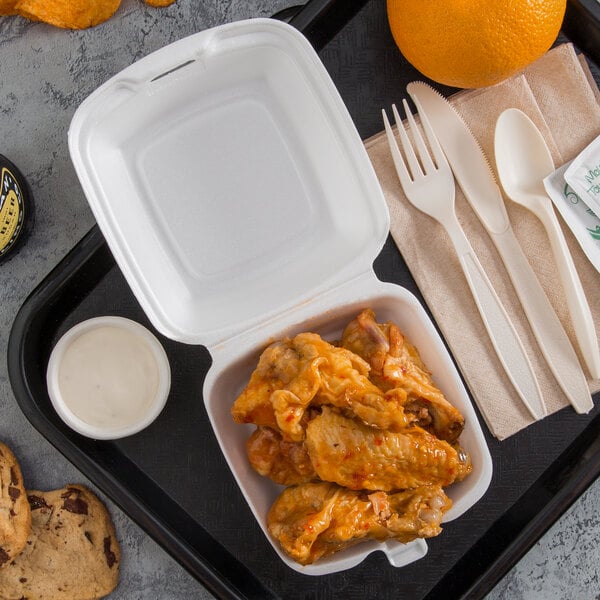 A white foam hinged lid container filled with food including chicken wings.