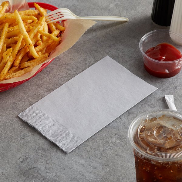 A basket of french fries next to a Choice silver and gray paper napkin and a drink.
