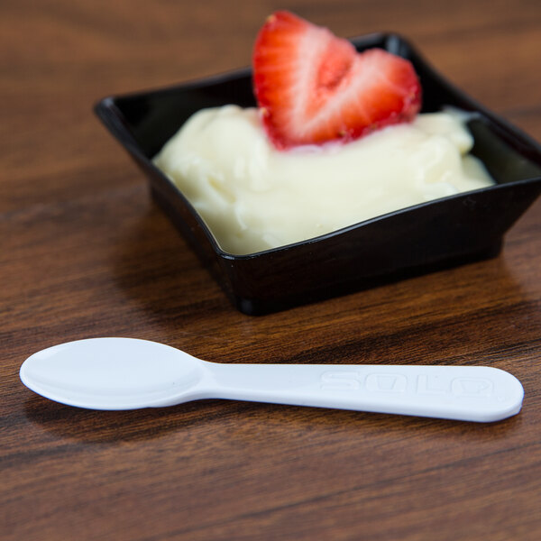 A white Solo taster spoon with a strawberry on top of a bowl of yogurt.