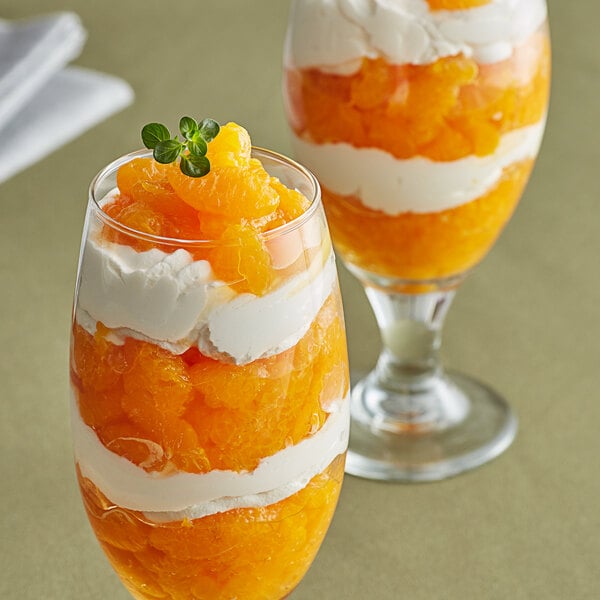 A glass of orange dessert with whipped cream and orange slices.