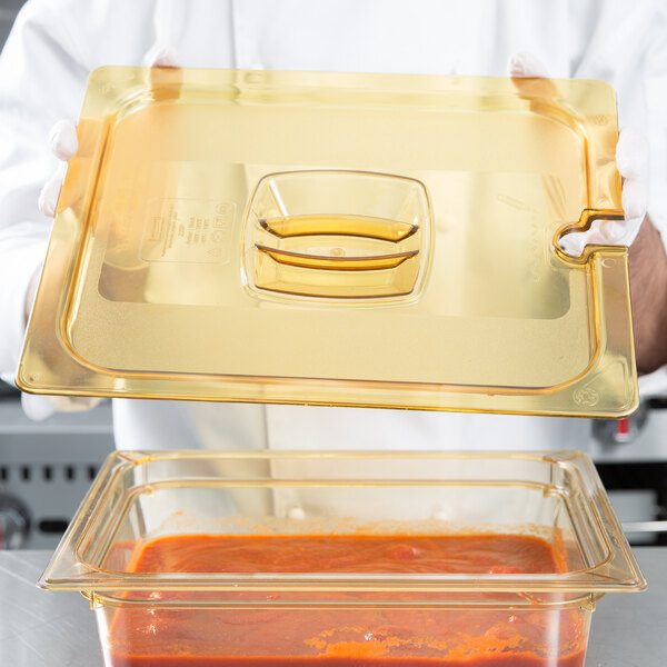 A chef using a Rubbermaid plastic food pan lid with handle to cover a tray of food.