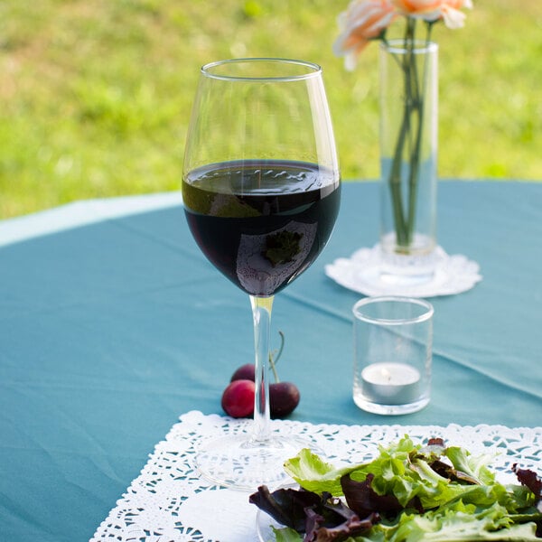 A Libbey tall wine glass filled with red wine on a table with a plate of salad.