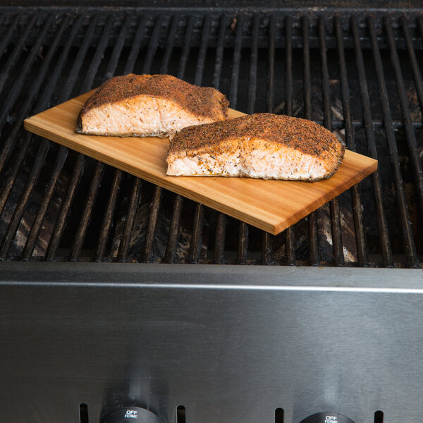 Two pieces of fish on a Chef Master cedar wood grilling plank on a grill.