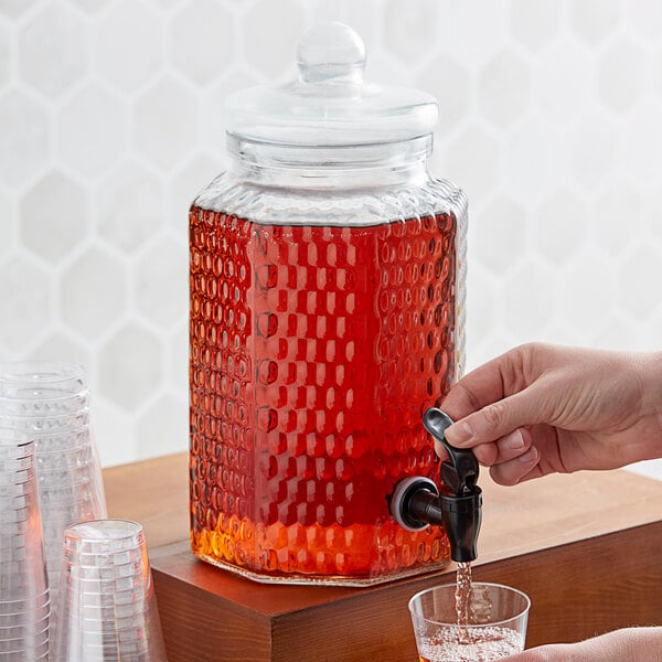 A person pouring red liquid into a glass from an Acopa glass beverage dispenser.