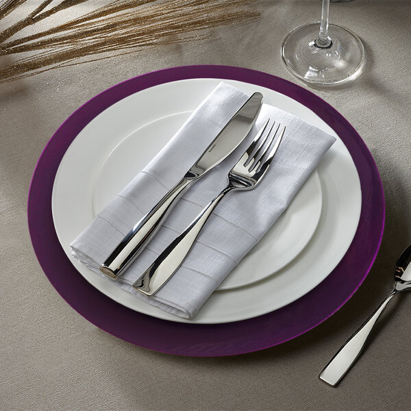 A purple Charge It by Jay plastic charger plate with silverware on a napkin.