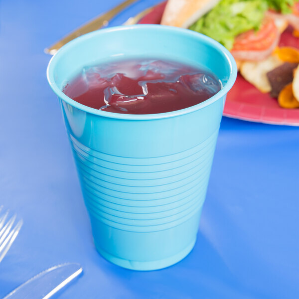 A Bermuda Blue plastic cup filled with a drink on a table next to a plate of food.