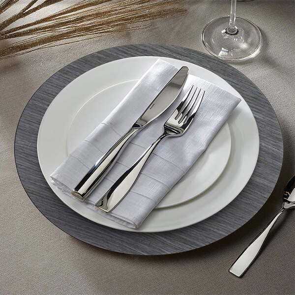 A gray faux wood charger plate with silverware on a white napkin.