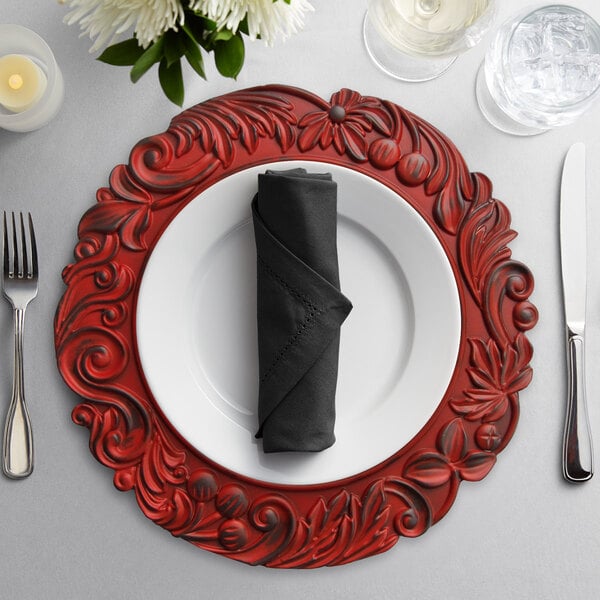 A place setting with a red oak charger plate, silverware, and a napkin on a table.