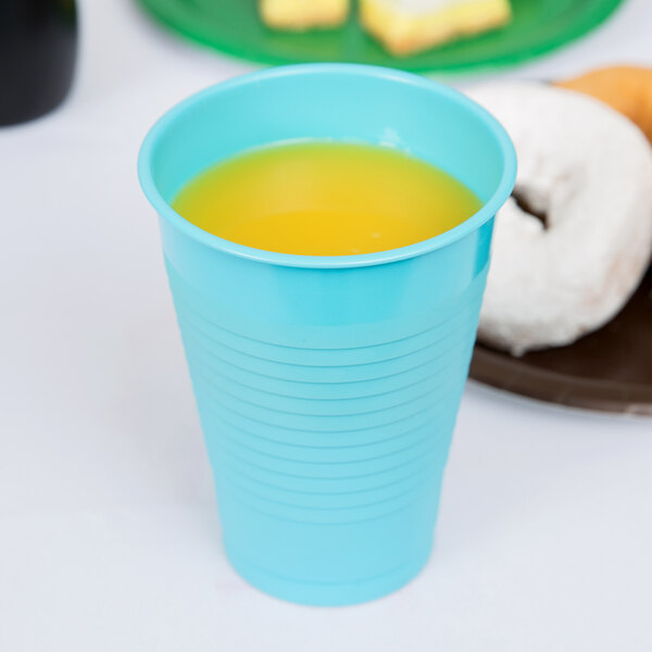 A blue Creative Converting plastic cup with orange liquid next to a white donut.